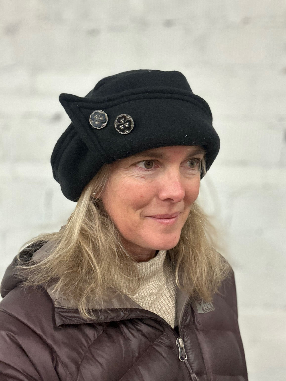 Woman wearing a black roll brim hat with two buttons on it, looking slightly away from the camera