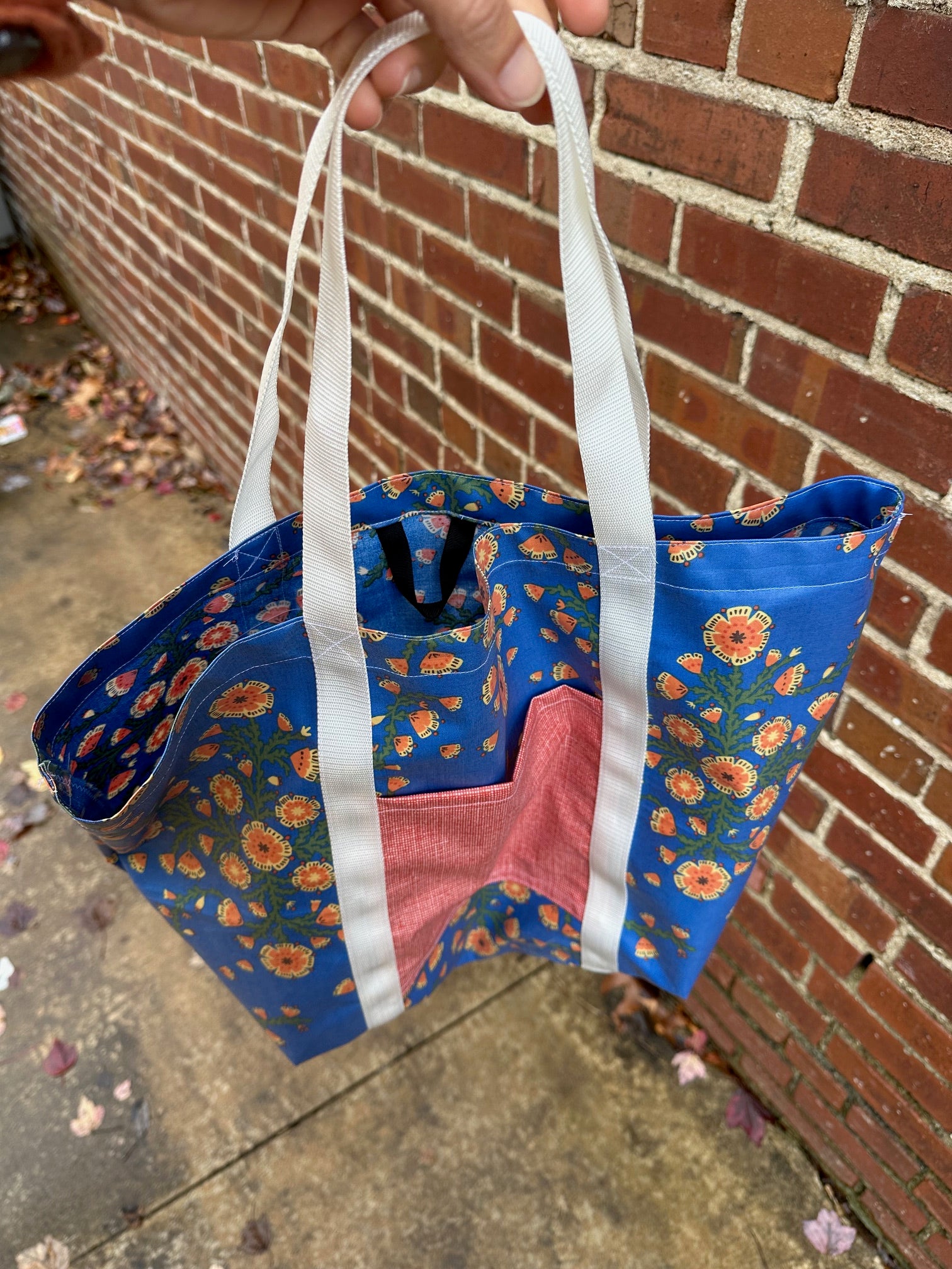 blue floral tote with red pocket and white straps, photo from above shows the black hang strap