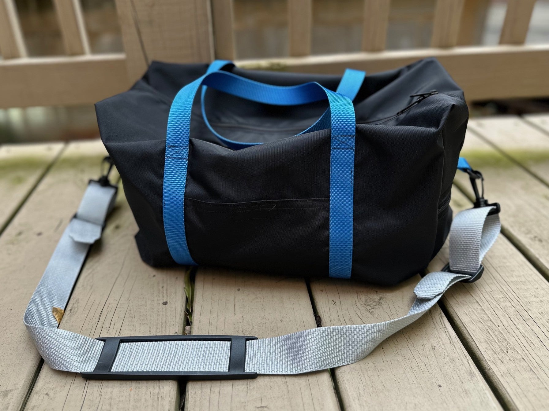 Black duffel bag with blue straps on a wooden deck