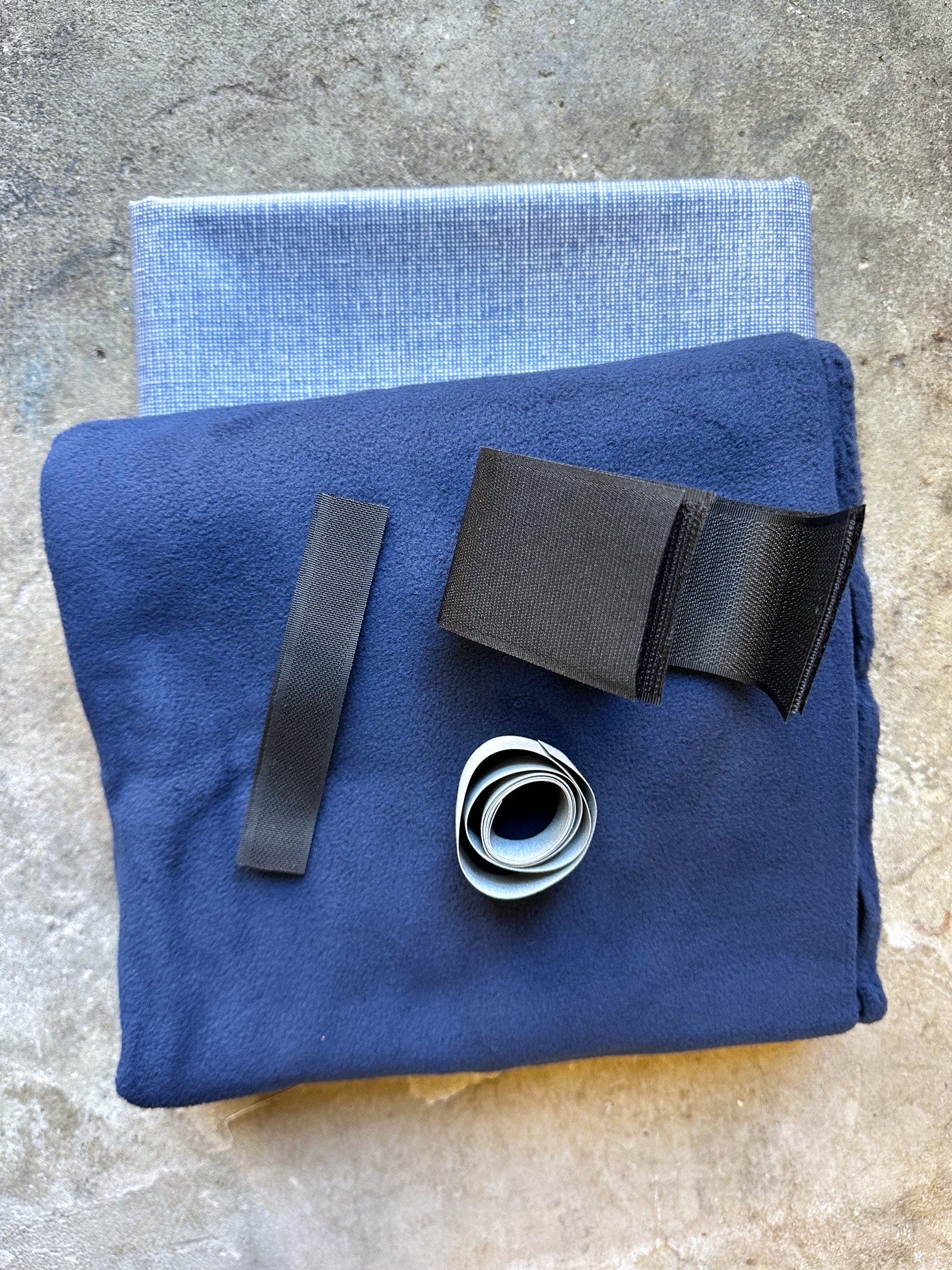 Blue fabric with black straps and a roll of tape on a textured surface