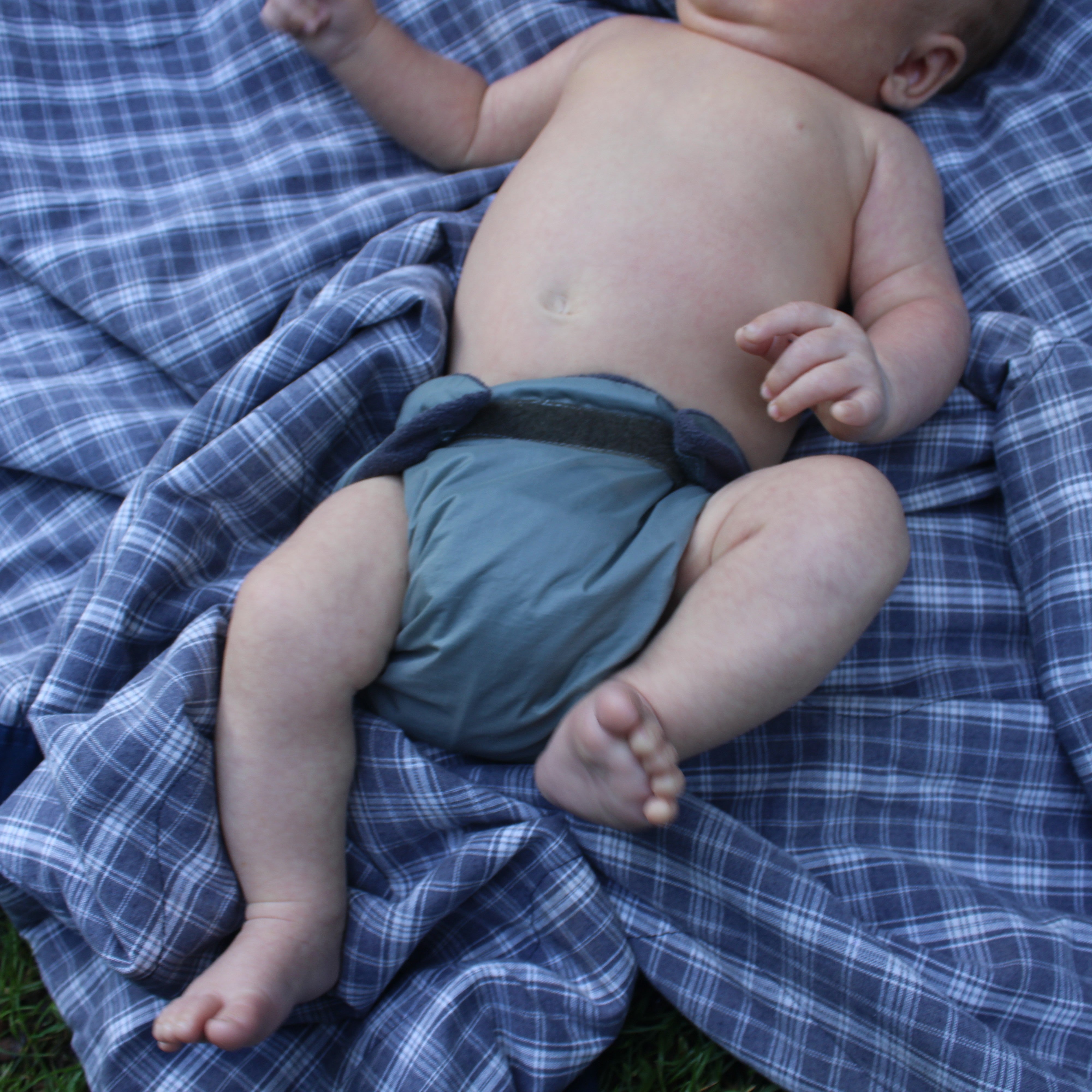 Baby wearing a cloth diaper on a blue plaid blanket outdoors