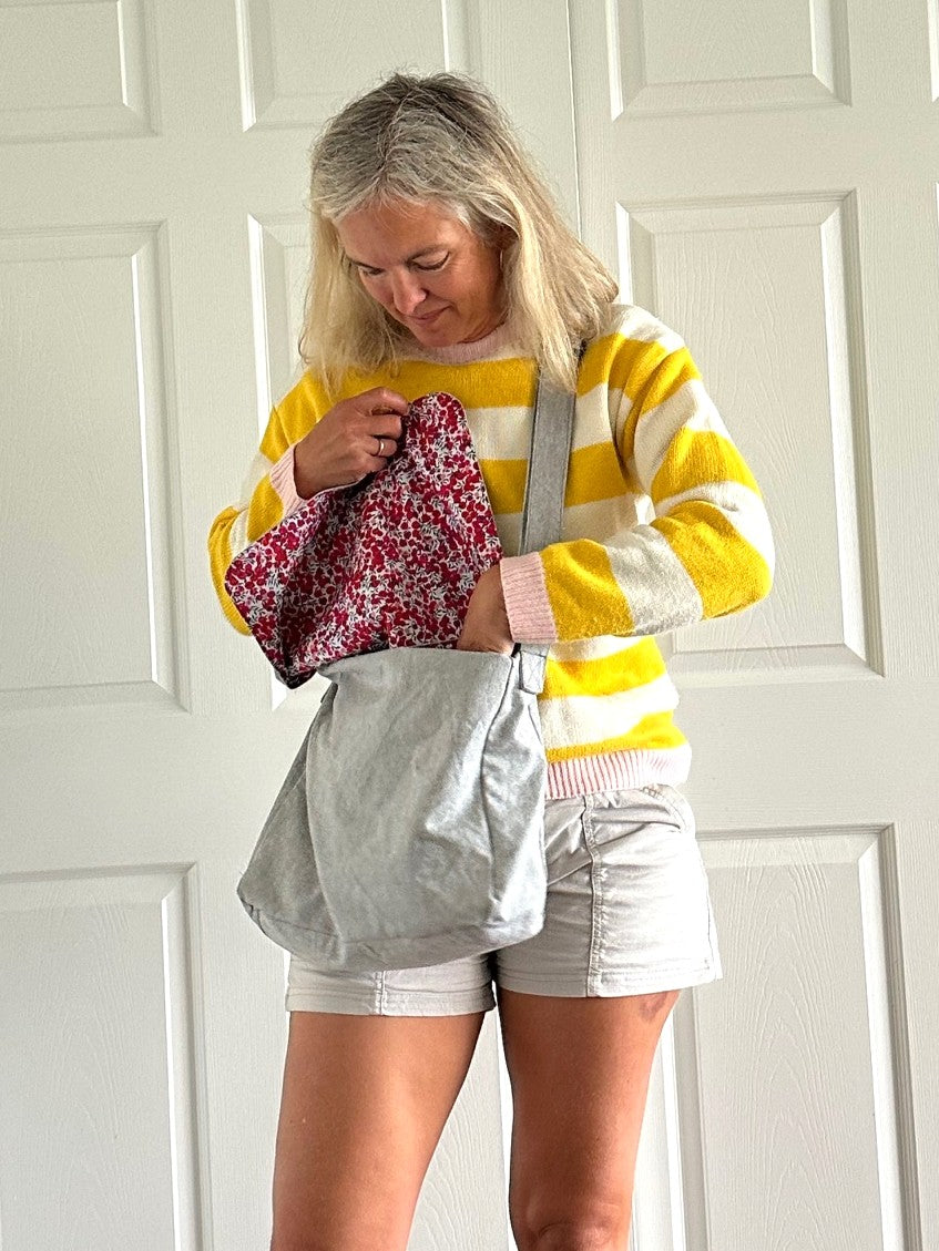 Woman wearing a yellow and white striped sweater with gray bag with  floral lining.