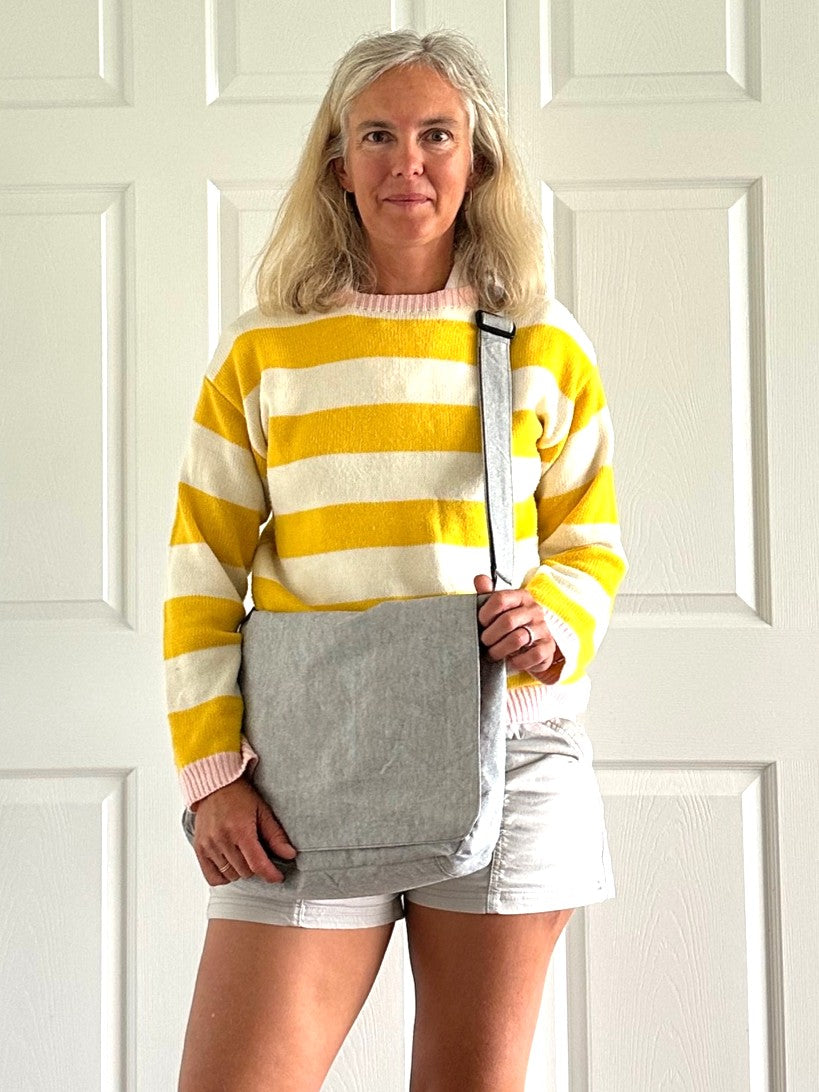 Woman wearing a yellow and white striped sweater with a gray courier bag against a white background