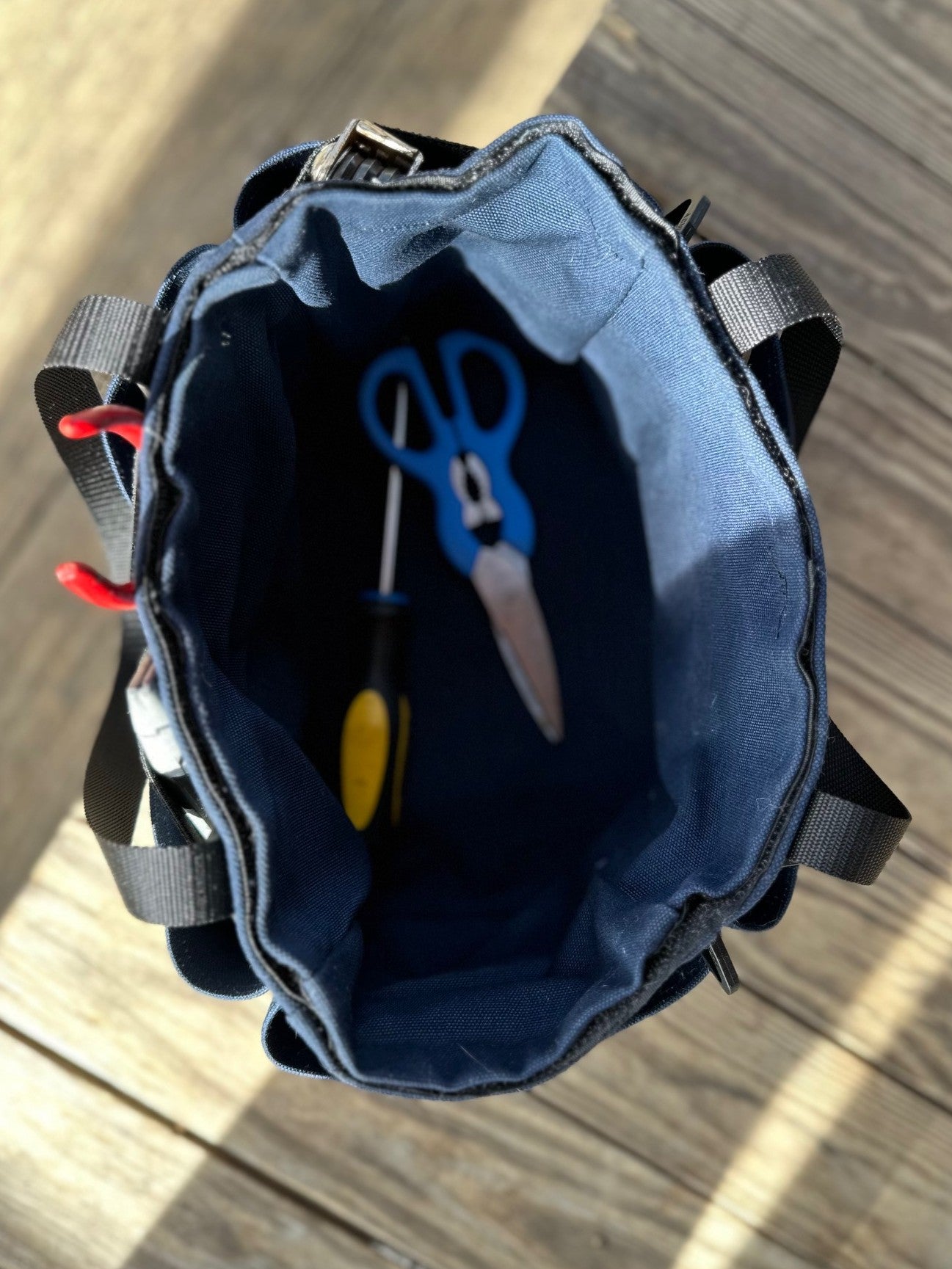 Open blue tool bag with tools inside on a wooden surface