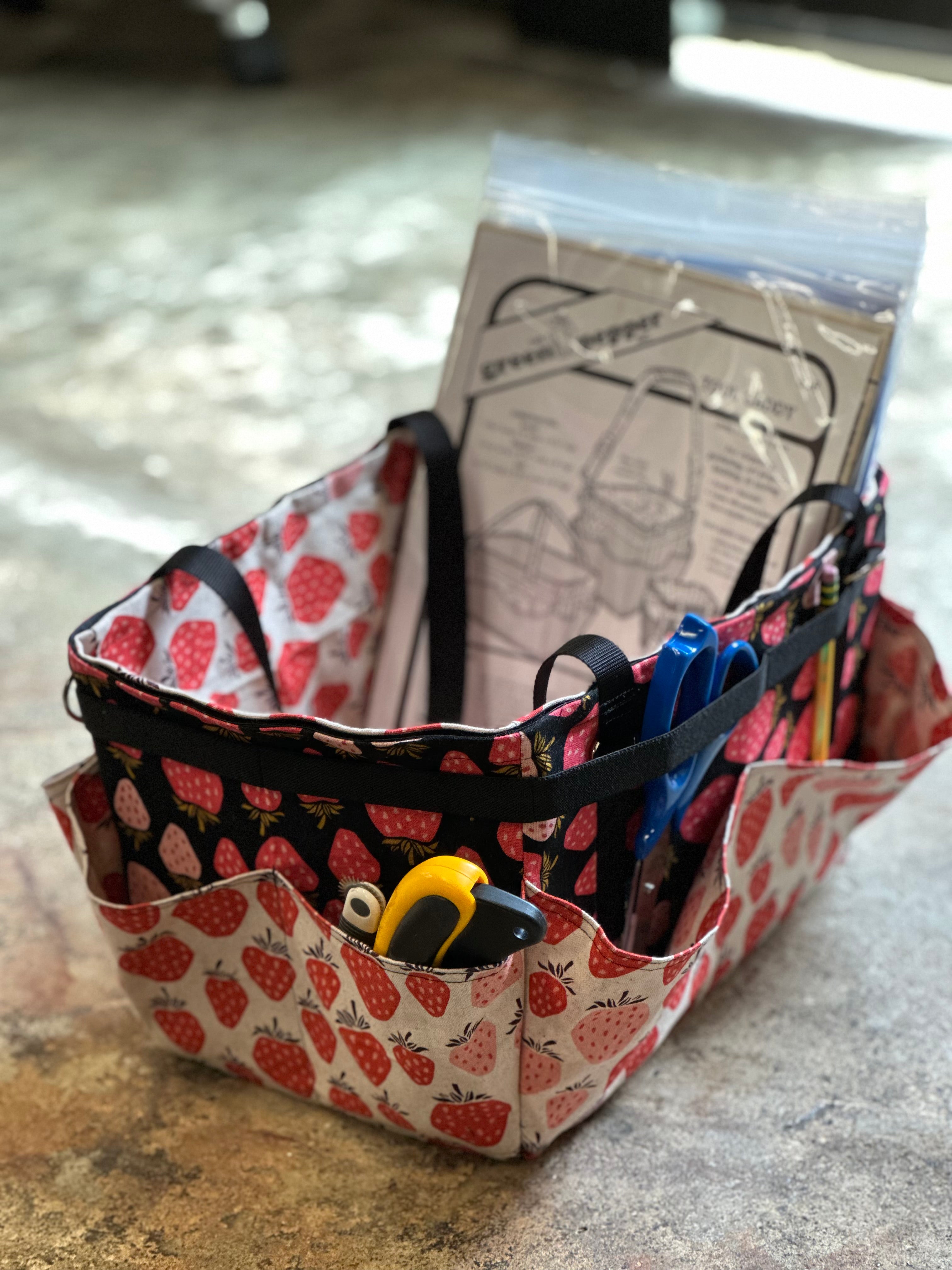 Fabric storage caddy with strawberry pattern holding scissors and other items on a countertop.