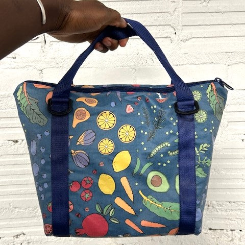 image of lunch tote made with blue fabric printed with vegetables and frult and with blue handles