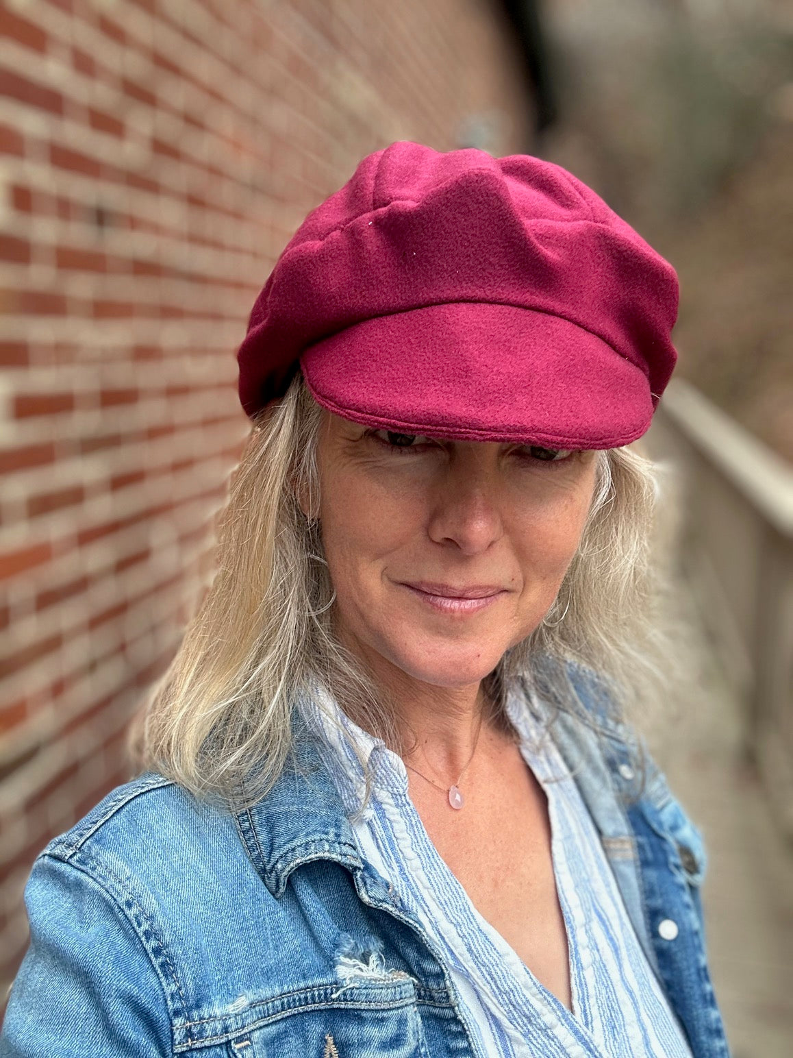 Person wearing a red beret and denim jacket against a brick wall.