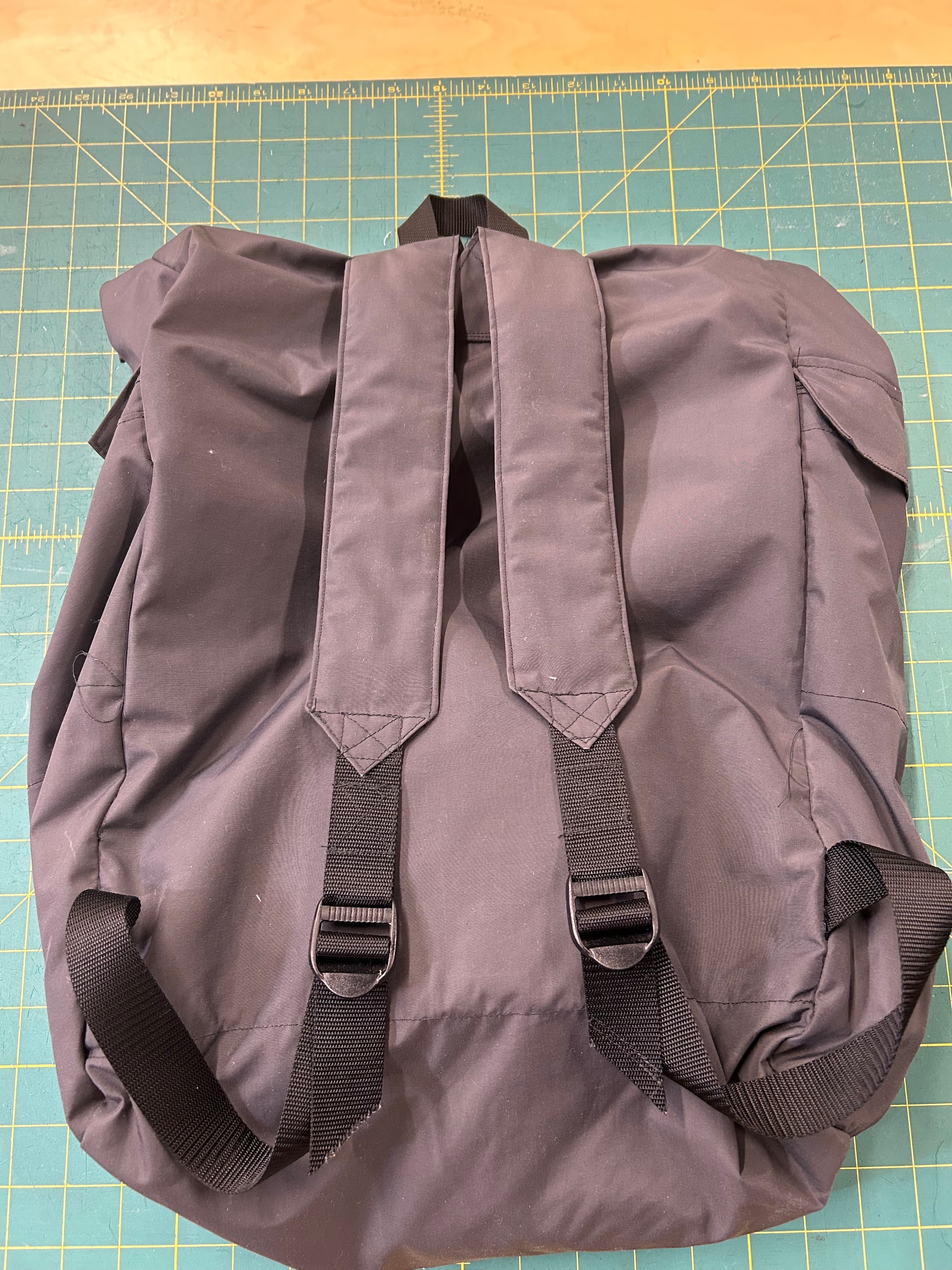 Gray back pack with strap side up on a grid background