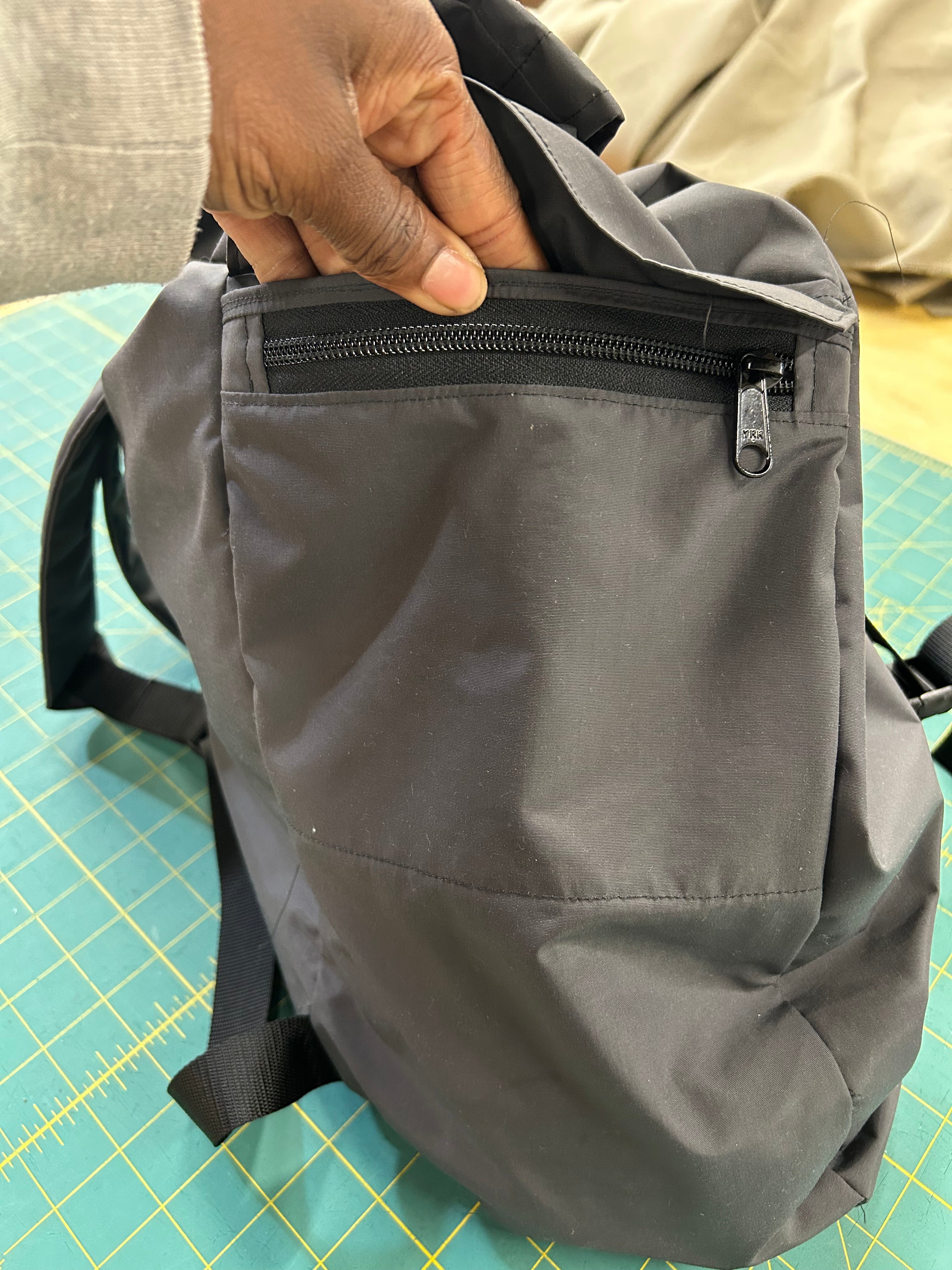 Gray backpack with a zipper held by a hand on a green cutting mat.