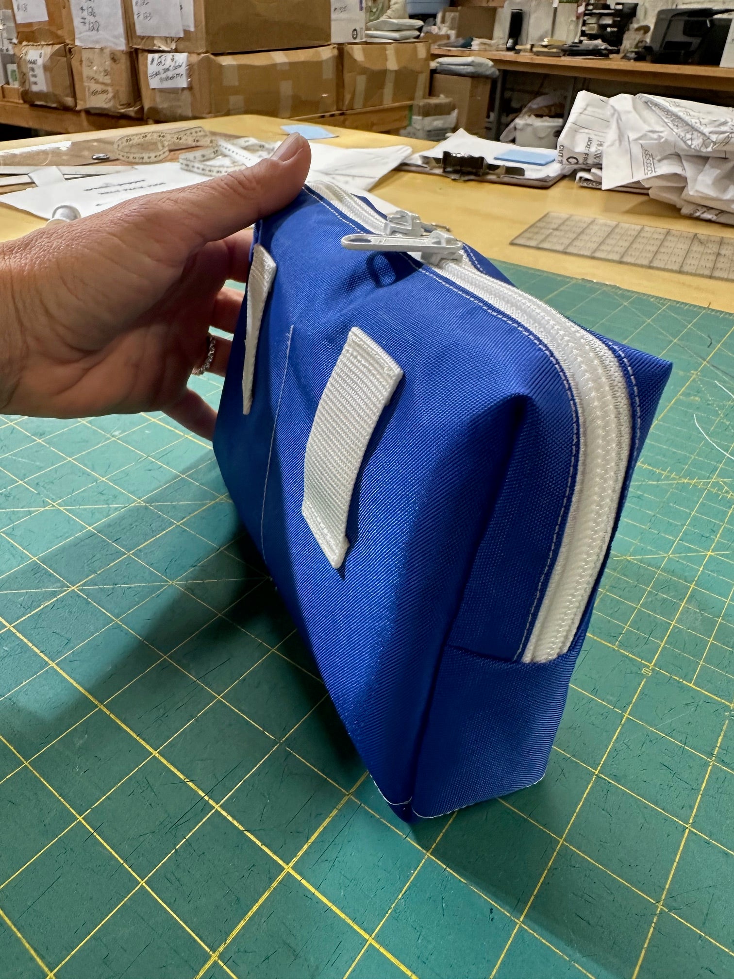 Blue pouch with a white zipper held by a hand on a green cutting mat.