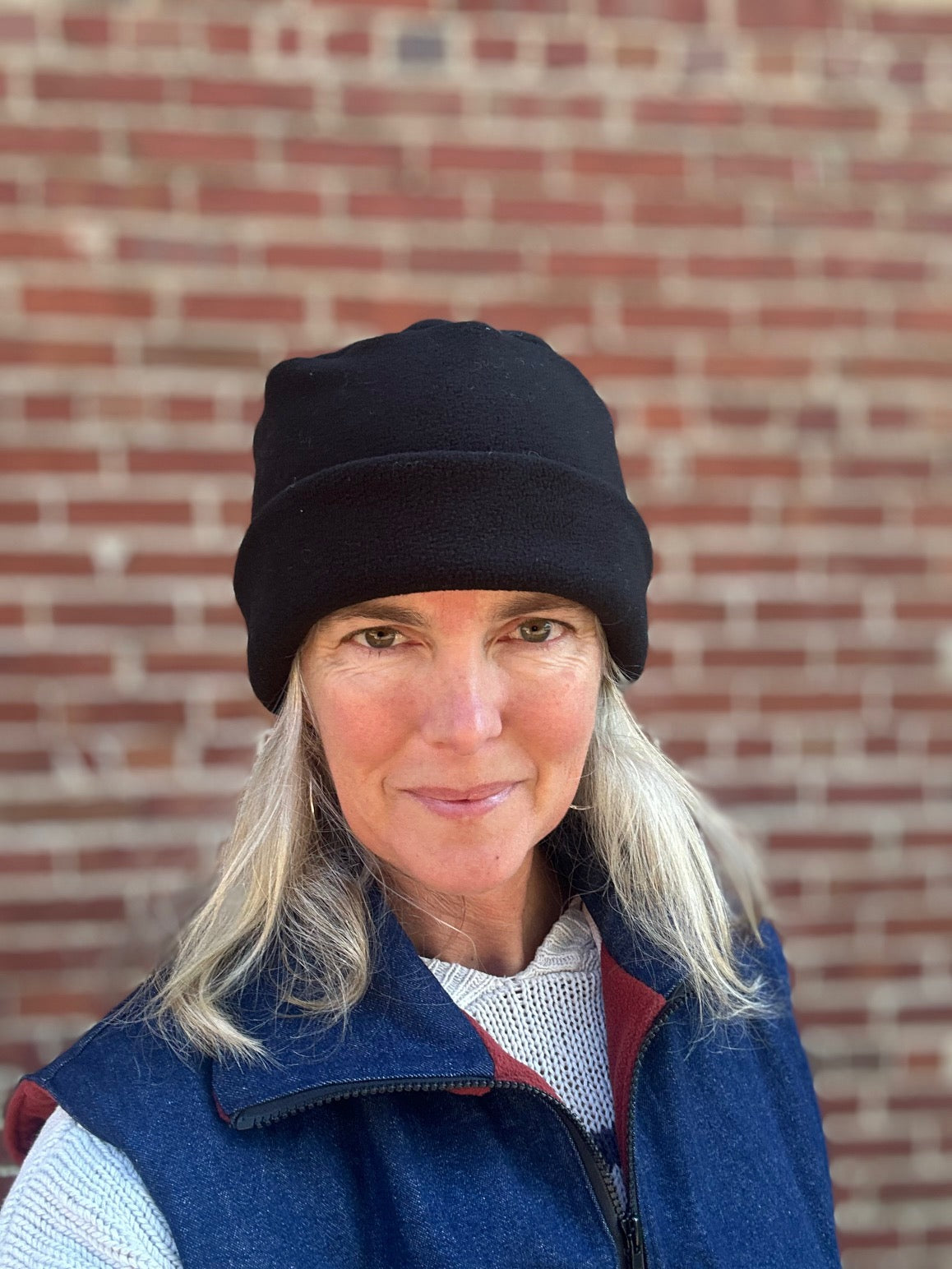 Person wearing a black arctic circle cap and blue vest against a brick wall