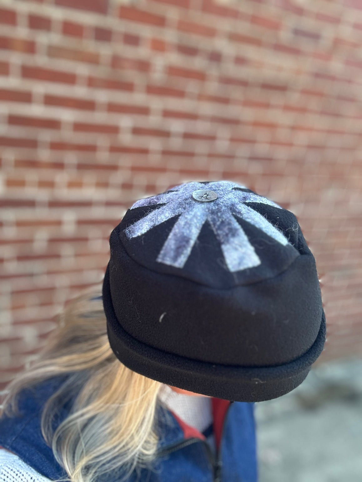 Black and white snowflake-patterned hat worn against a brick wall.