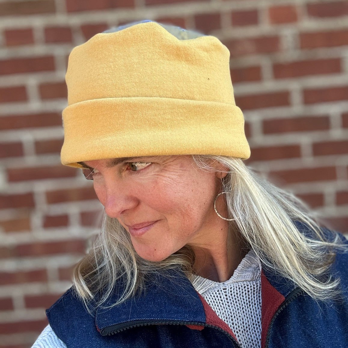 Person wearing a yellow cap and blue jacket against a brick wall