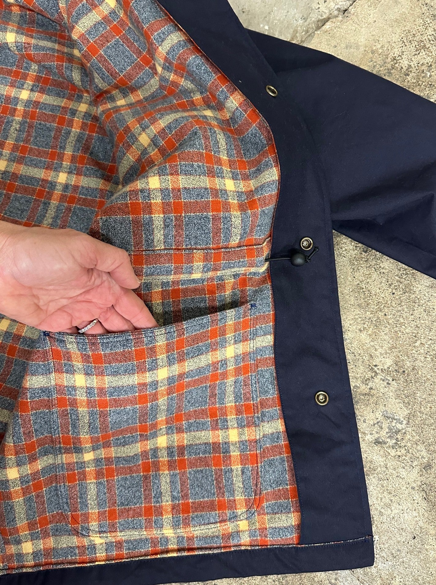 Close-up of a plaid jacket with a hand reaching into the pocket on a concrete surface.