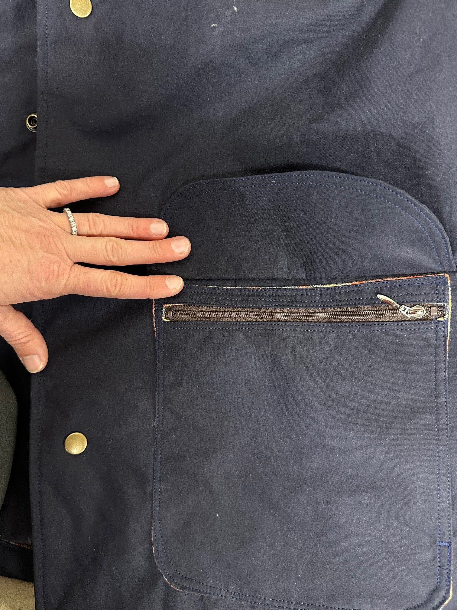 Close-up of a navy blue jacket with a hand touching the chest pocket.