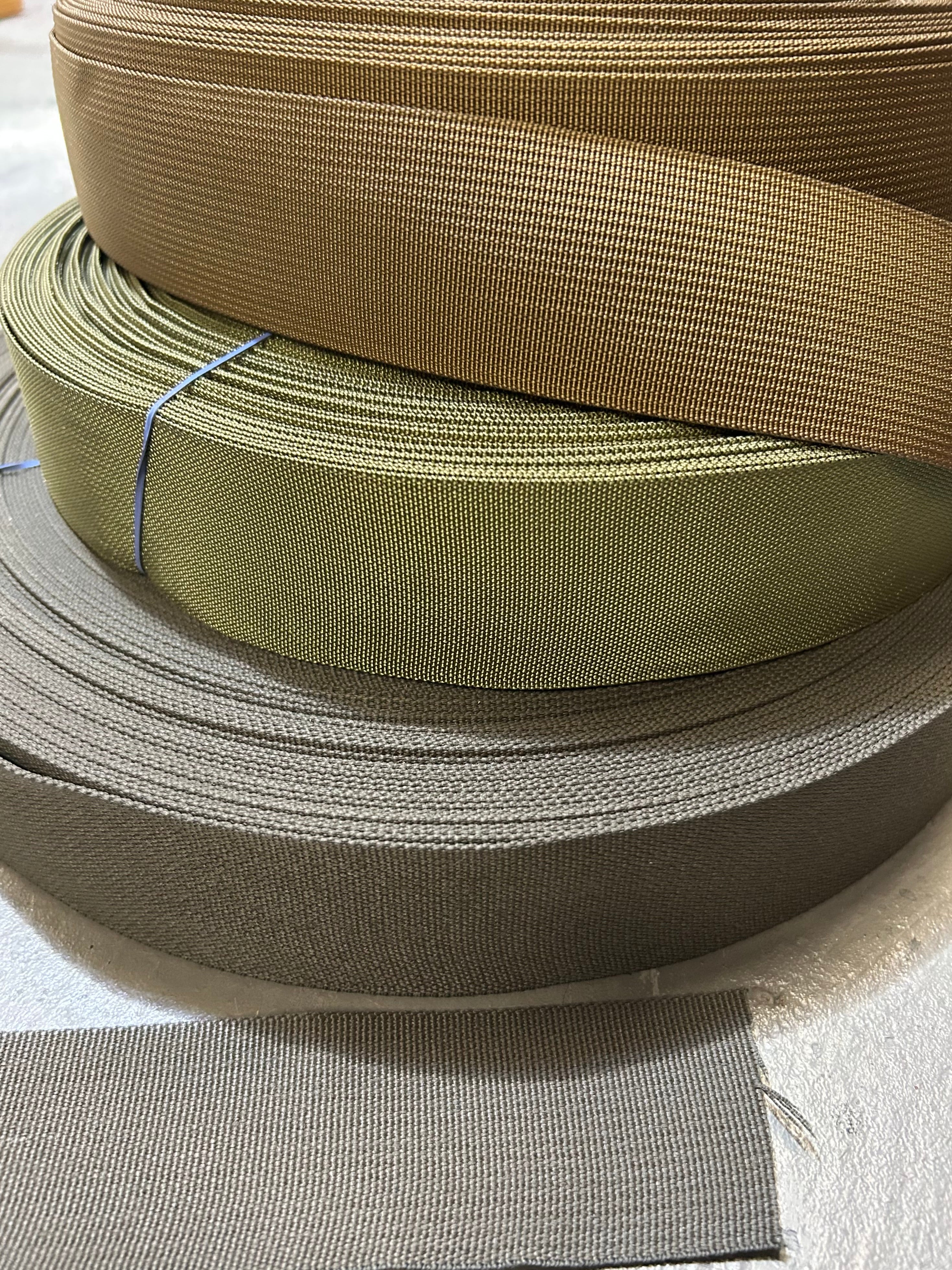 Stack of brown, green, and gray webbing strips on a light gray background