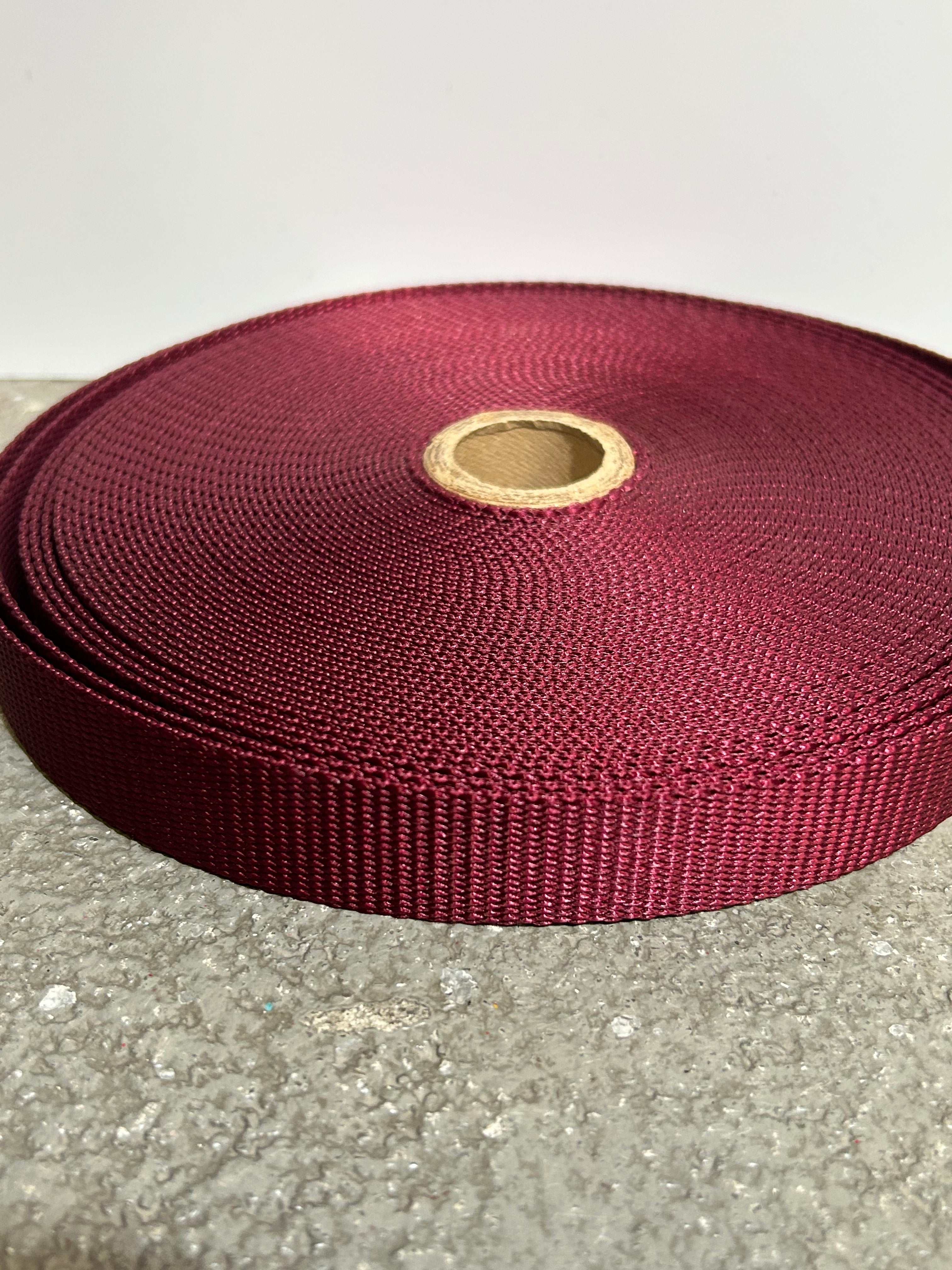 Roll of burgundy webbing on a concrete surface