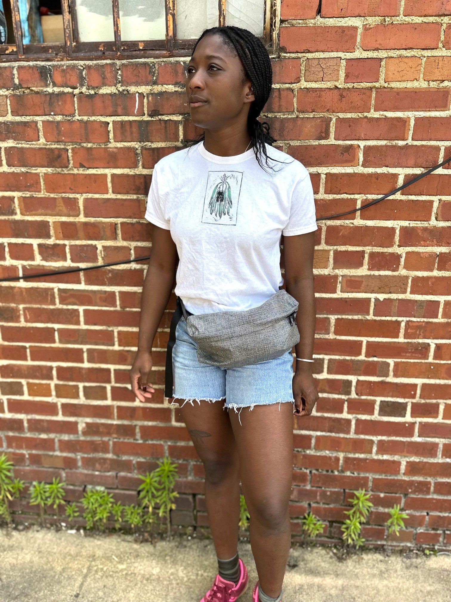 Person wearing a white t-shirt and denim shorts standing against a brick wall.