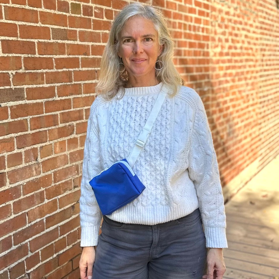 Woman wearing a white sweater and blue crossbody bag against a brick wall.
