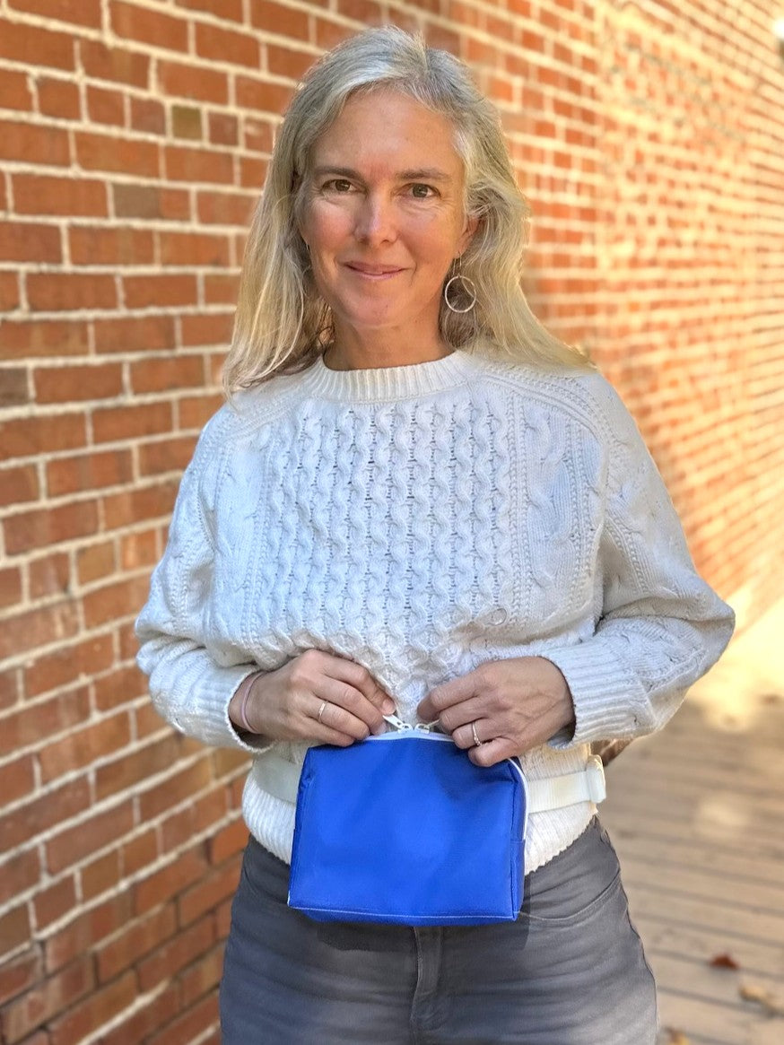 Woman wearing a white sweater holding a blue pouch against a brick wall.