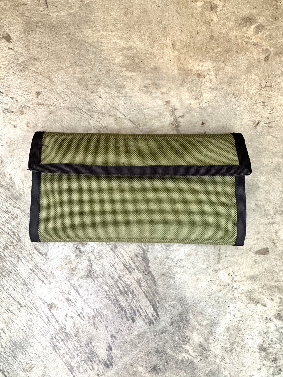 green checkbook wallet with black trim on a concrete floor