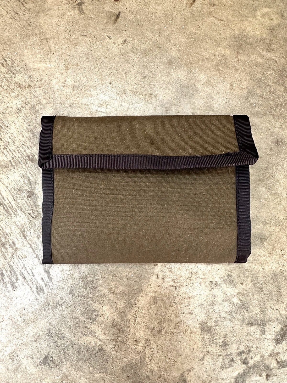 Small olive colored wallet with black trim on a concrete floor