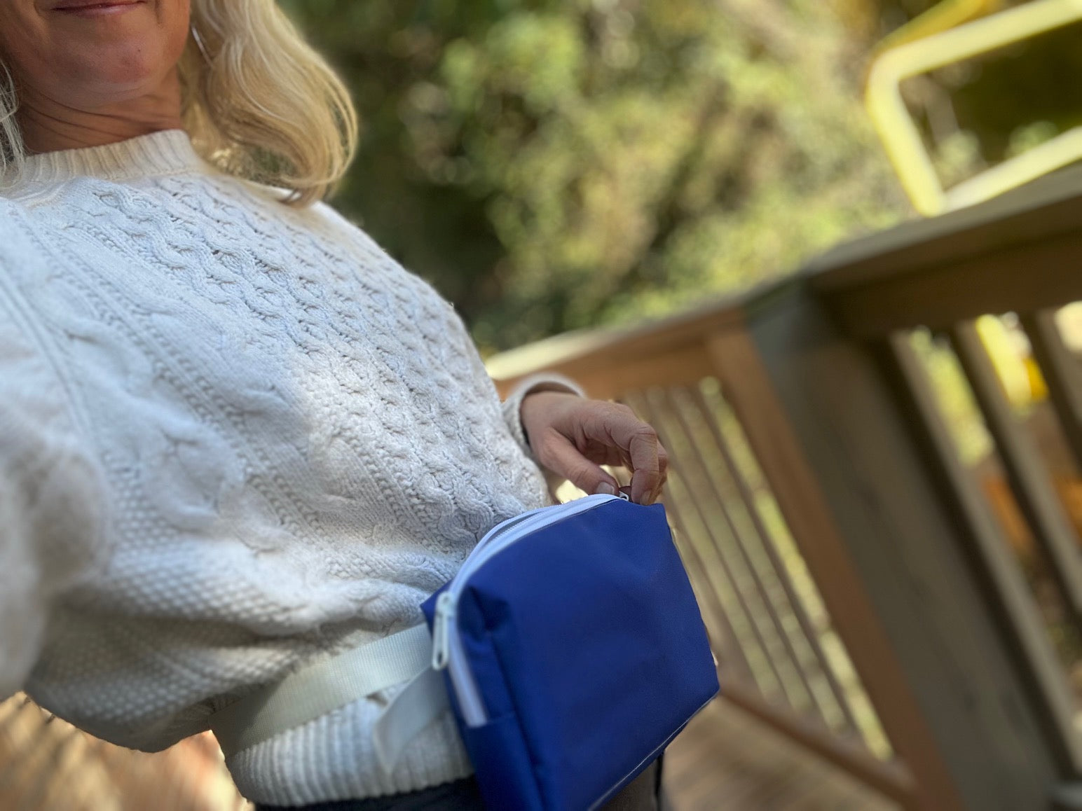 Person wearing a white sweater holding a blue bag outdoors
