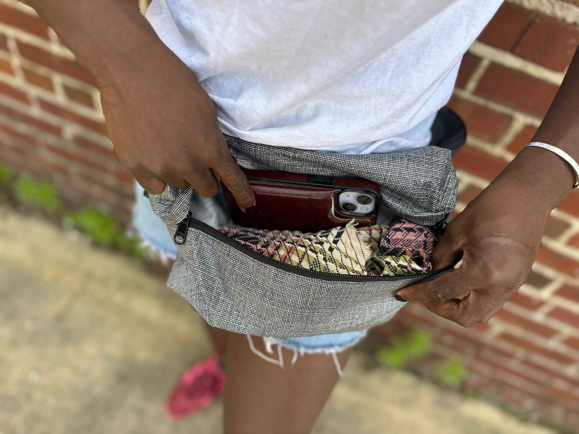 Person wearing a gray waist bag with a brick wall background