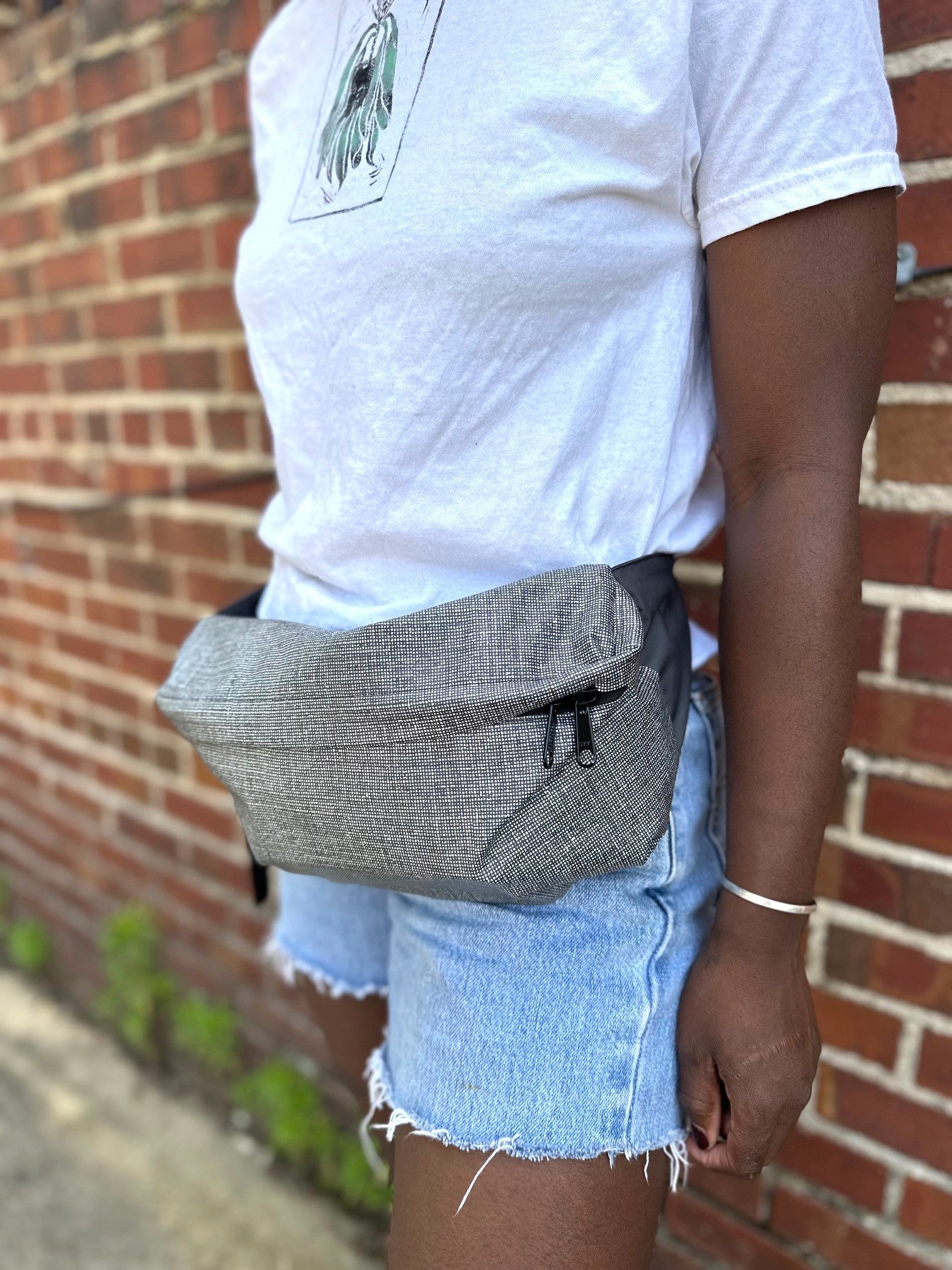 Person wearing a gray waist bag against a brick wall